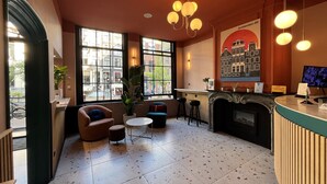 A spacious lobby with a fireplace, comfortable seating, and large windows offering city views. - Heart Of Amsterdam - Hostel (Amsterdam)