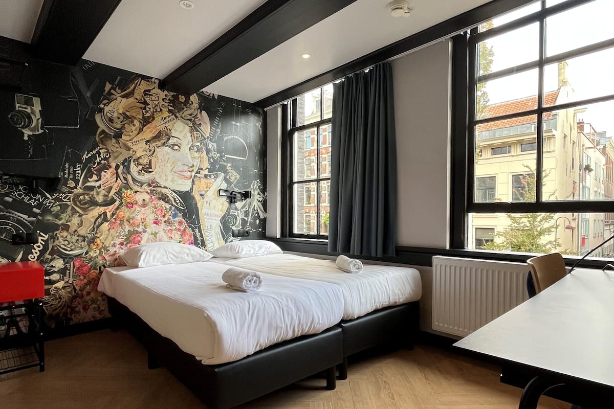 A modern bedroom with a bed, a desk, and a large window.