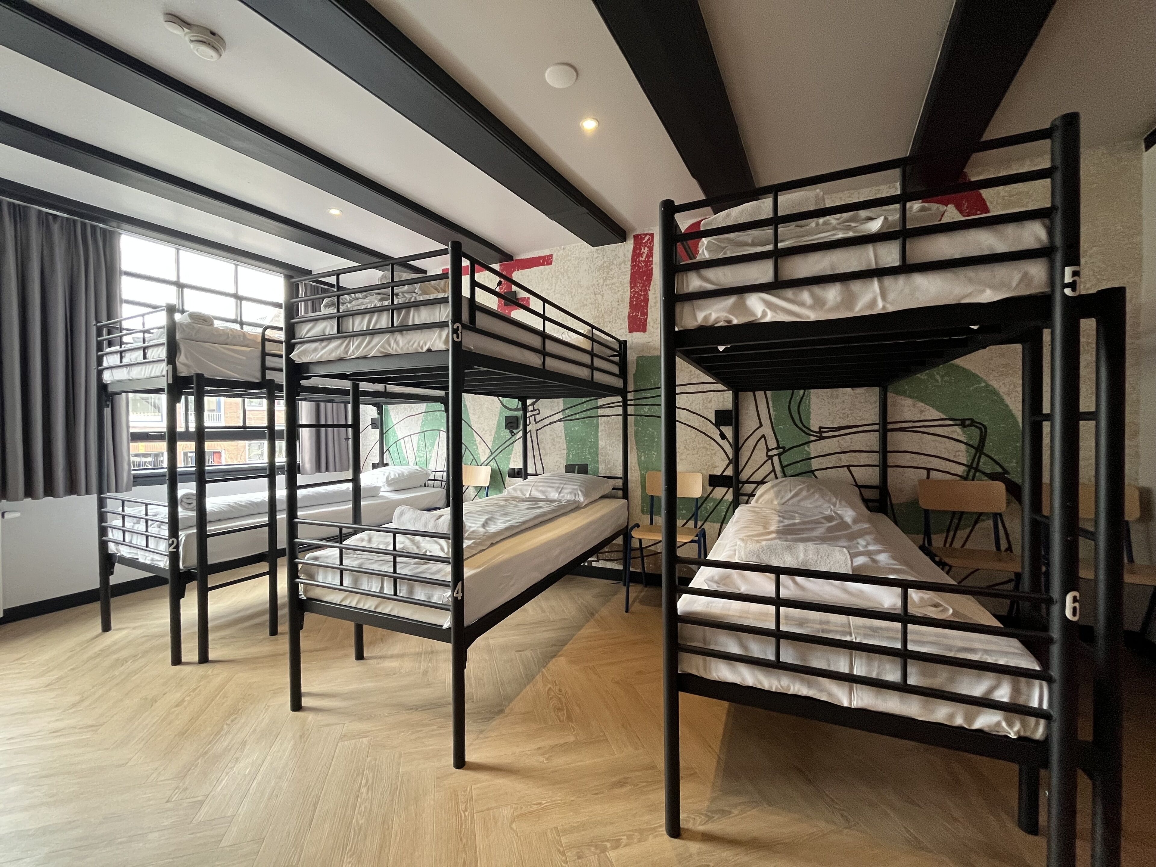 Camas literas en una habitación con ventana, suelo de madera y decoración roja en la pared.