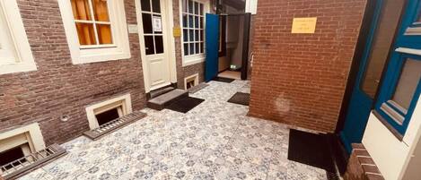 Un pasillo con baldosas de piso estampadas, pared de ladrillo y puerta azul.