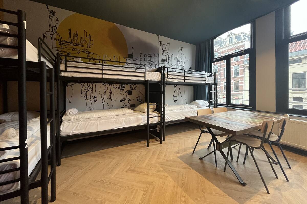 A dormitory room with bunk beds, a wooden table, and chairs.