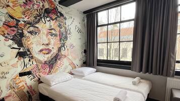 Habitación de hotel con dos camas, un mural grande en la pared, una ventana con cortinas y un radiador.