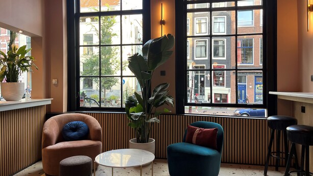 A cozy interior with a seating area, large windows, and a view of the city. - Heart Of Amsterdam - Hostel (Amsterdam)