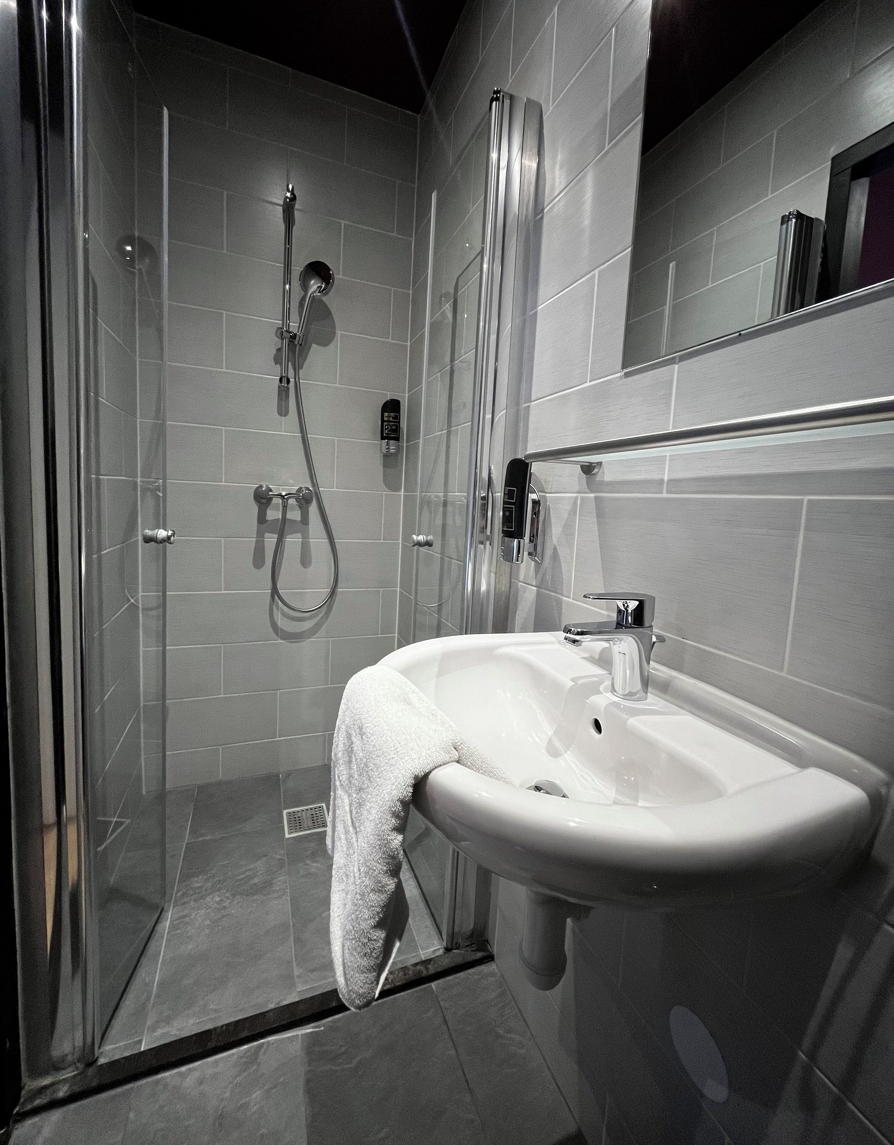 Un bany modern amb una cabina de dutxa de vidre, un lavabo blanc i un mirall damunt del lavabo.