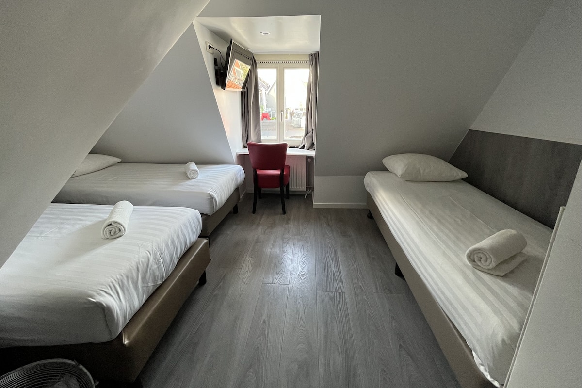 A small, triangular room with two single beds, a desk, and a chair.