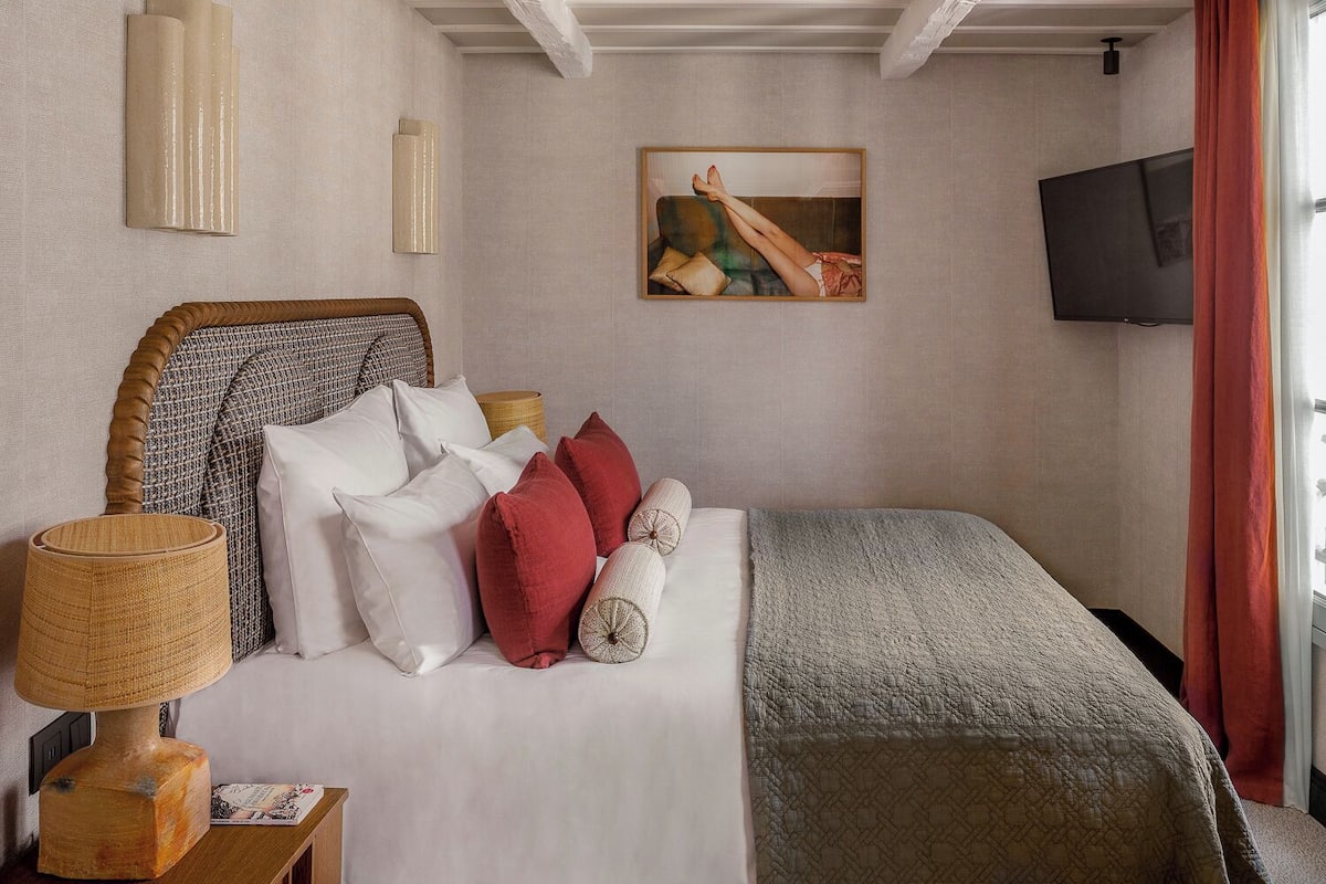 Habitación de hotel ordenada con cama, televisor, un cuadro y una lámpara.