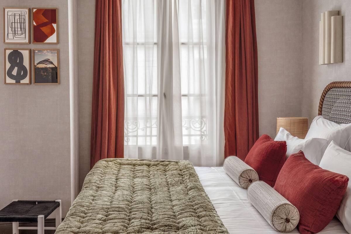 Un dormitorio con cama, una banca y cortinas.