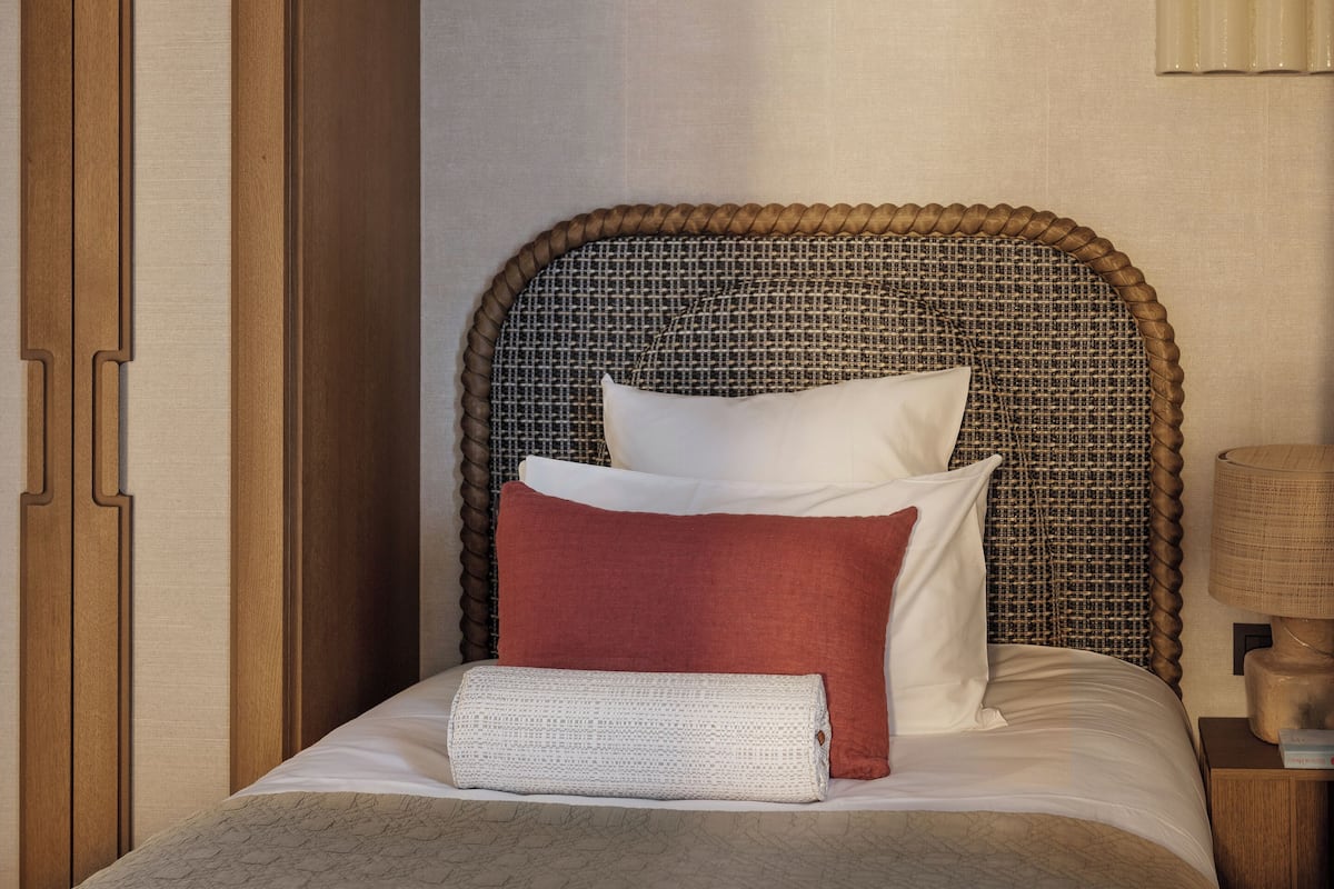 Una cama bien hecha con un cabecero tejido, un armario de madera y una mesita de noche con lámpara.