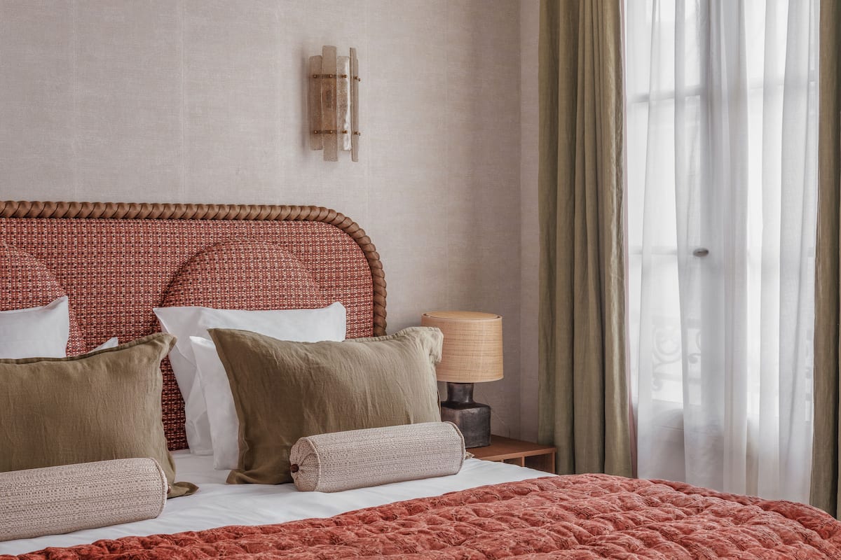 Una cama bien hecha con un edredón rojo, un cabecero tejido y varias almohadas.