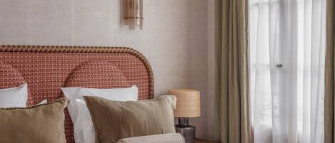 A neatly made bed with a red blanket, a woven headboard, and several pillows.