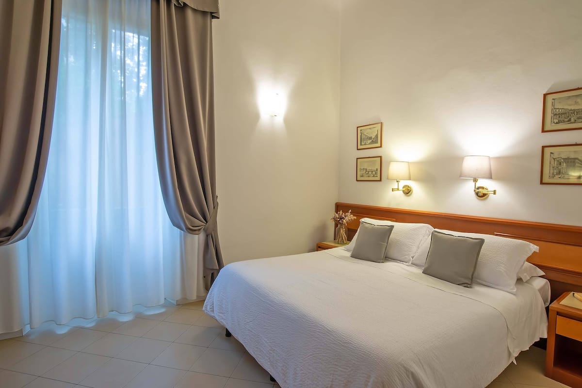Una habitación de hotel con una cama grande, una mesita de noche con una lámpara y un aplique en la pared.