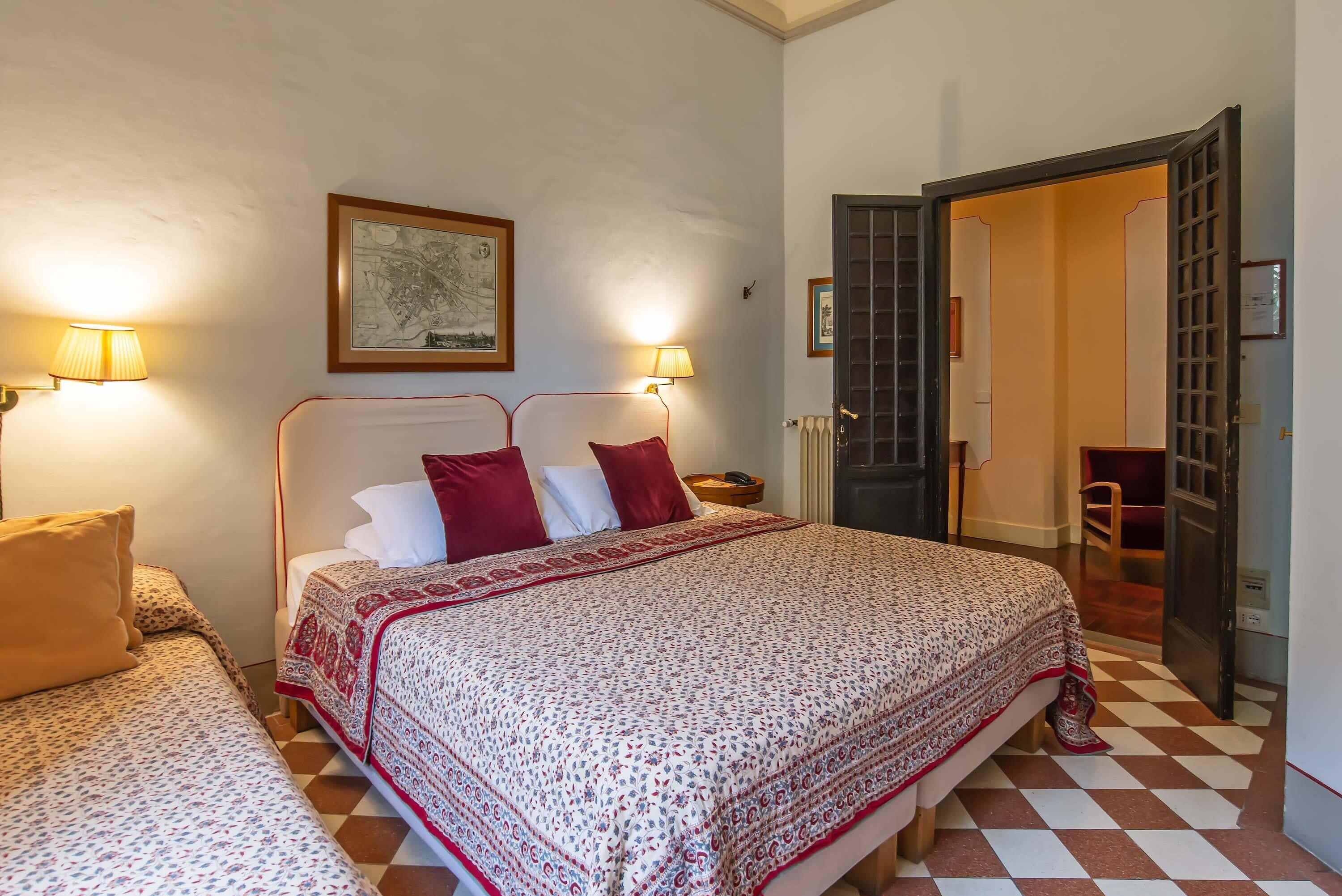 Une chambre d’hôtel avec un grand lit, deux tables de chevet, une chaise et une porte donnant sur une autre pièce.