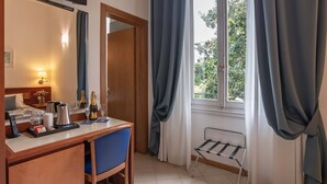 Une chambre d’hôtel équipée d’un bureau, d’une chaise, d’un lit et d’une fenêtre avec des rideaux.
