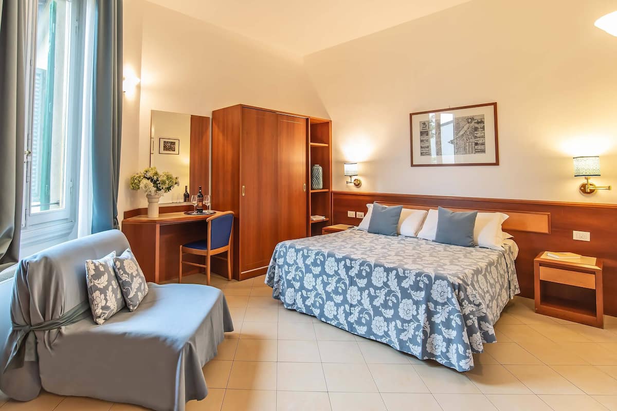 Una habitación de hotel con una cama, un escritorio, una silla, un armario y una mesita de noche.