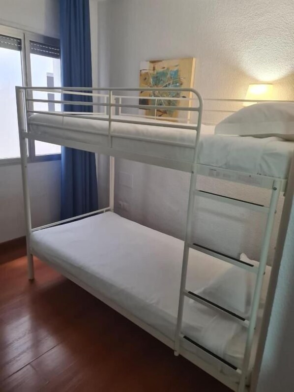 Uma cama de solteiro em um quarto com janela, um quadro na parede e uma luminária.