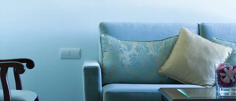 A living room with a blue sofa, a wooden chair, a lamp, and a framed picture on the wall.