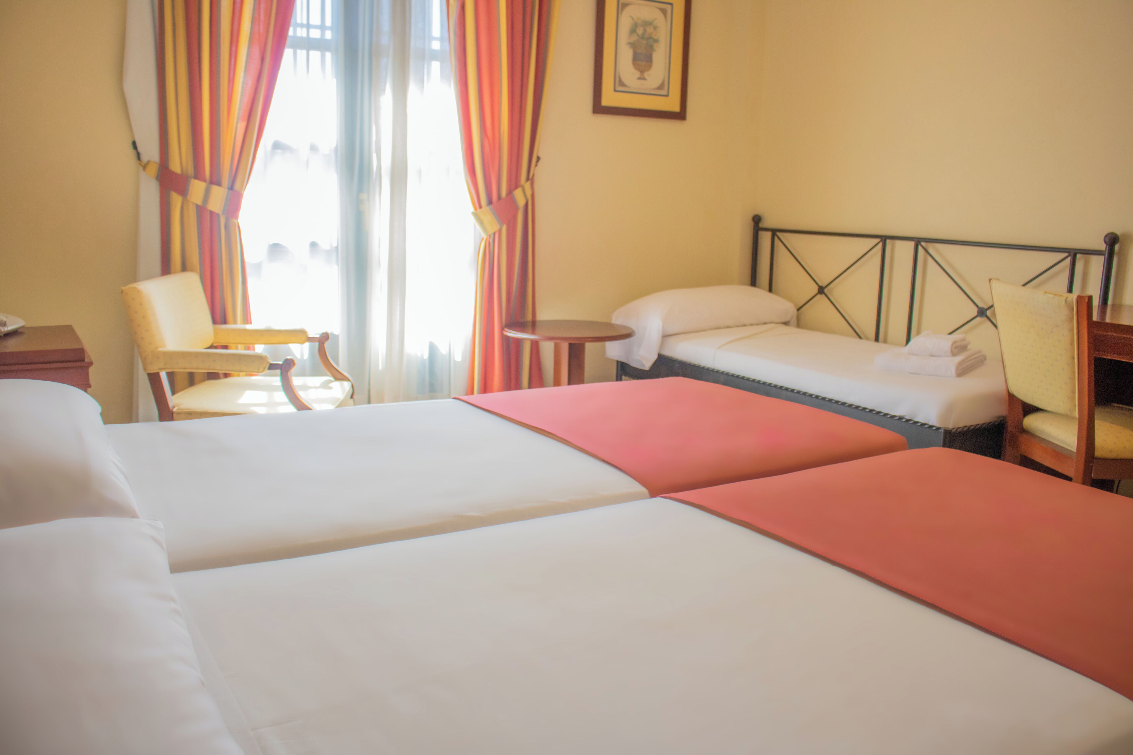 A hotel room with two beds, a chair, a small table, and curtains.
