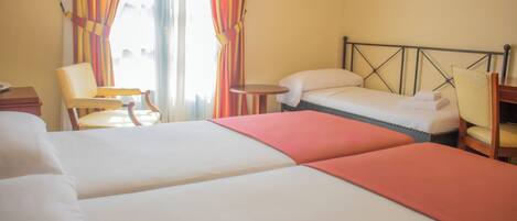 A hotel room with two beds, a chair, a small table, and curtains.