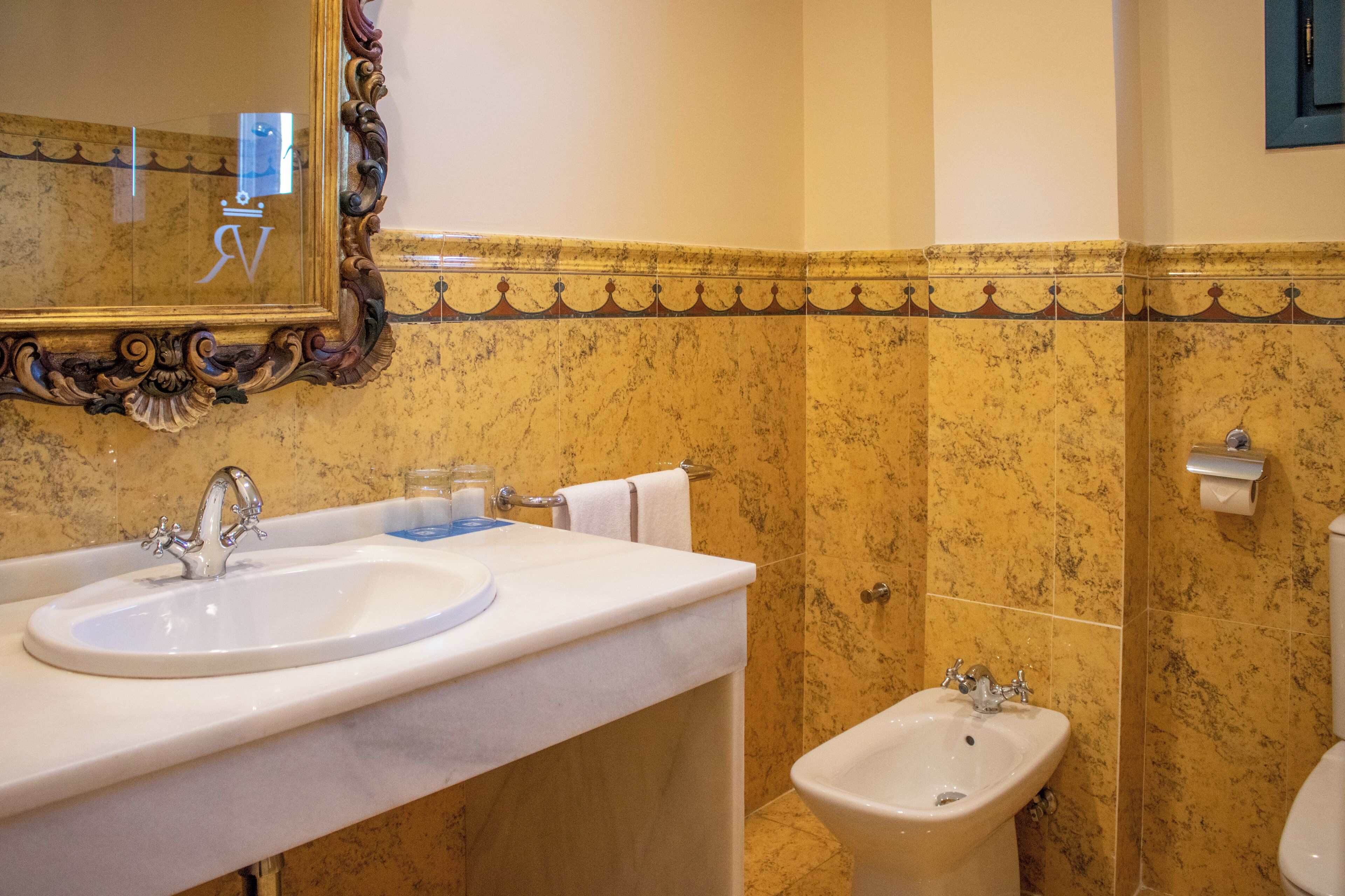 Un baño con lavamanos de mármol, un bidé y un espejo con un marco decorativo.