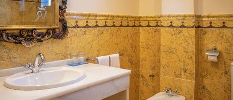 Un baño con lavamanos de mármol, un bidé y un espejo con un marco decorativo.
