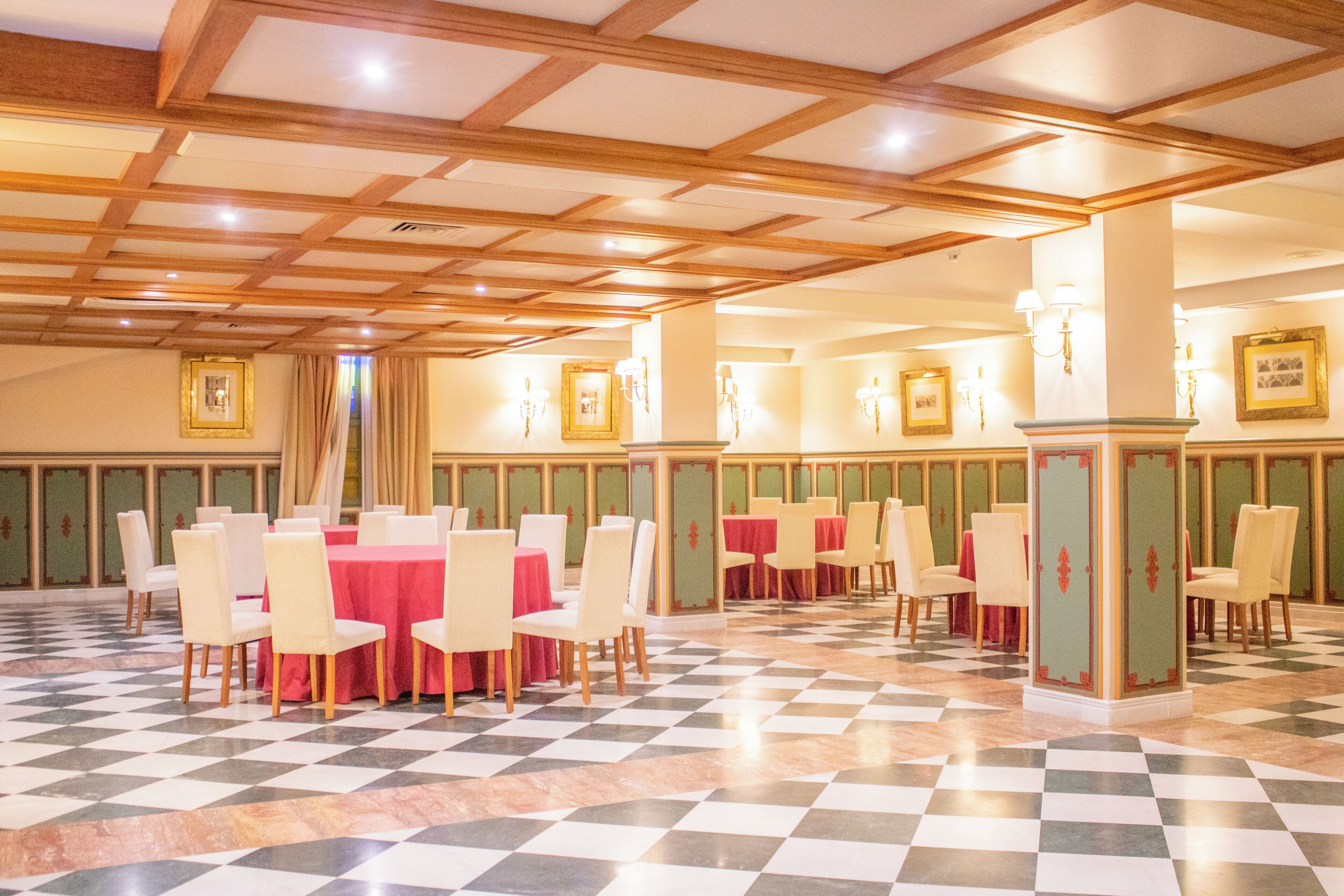 A banquet hall with checkered flooring, multiple tables with red tablecloths, and chairs.