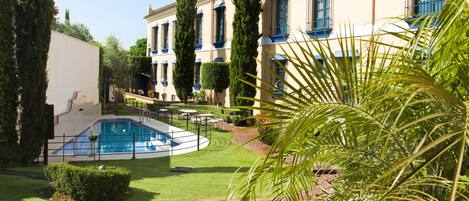 A pool area with a circular design, surrounded by a well-maintained lawn and a brick pathway.