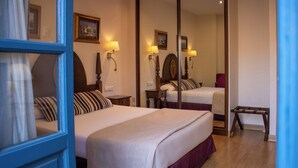 Habitación de hotel con dos camas, un espejo grande, lámparas de noche y un pequeño banco.