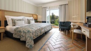 Habitación de hotel con una cama grande, un escritorio, una silla y un balcón con cortinas.