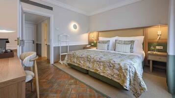 Quarto de hotel com cama, mesas de cabeceira, uma cadeira, escrivaninha e porta.