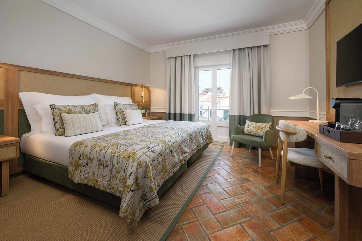 A hotel room with a large bed, a desk with a chair, a television, and a window with curtains.