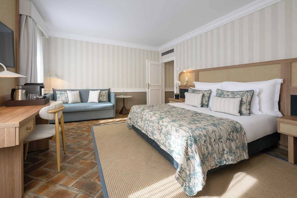 A hotel room with a bed, a sofa, a desk, and a small table.