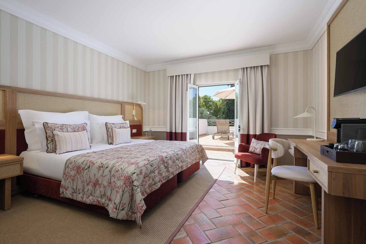 A hotel room with a large bed, a desk with a chair, a TV, and a view of the outdoors.