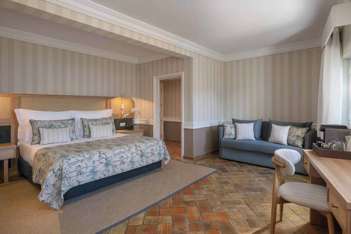 A hotel room with a bed, a sofa, a chair, and a small table.