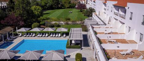 Zona de piscina en la azotea con sillones de descanso y sombrillas, rodeada de edificios blancos con tejados rojos.