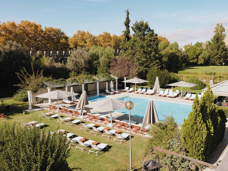 A pool area with lounge chairs and umbrellas, surrounded by trees and a stone wall.