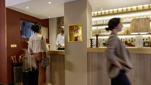 A hotel reception area with a counter, a framed artwork, and a display of bottles. - Hotel Bailli de Suffren (Paris)