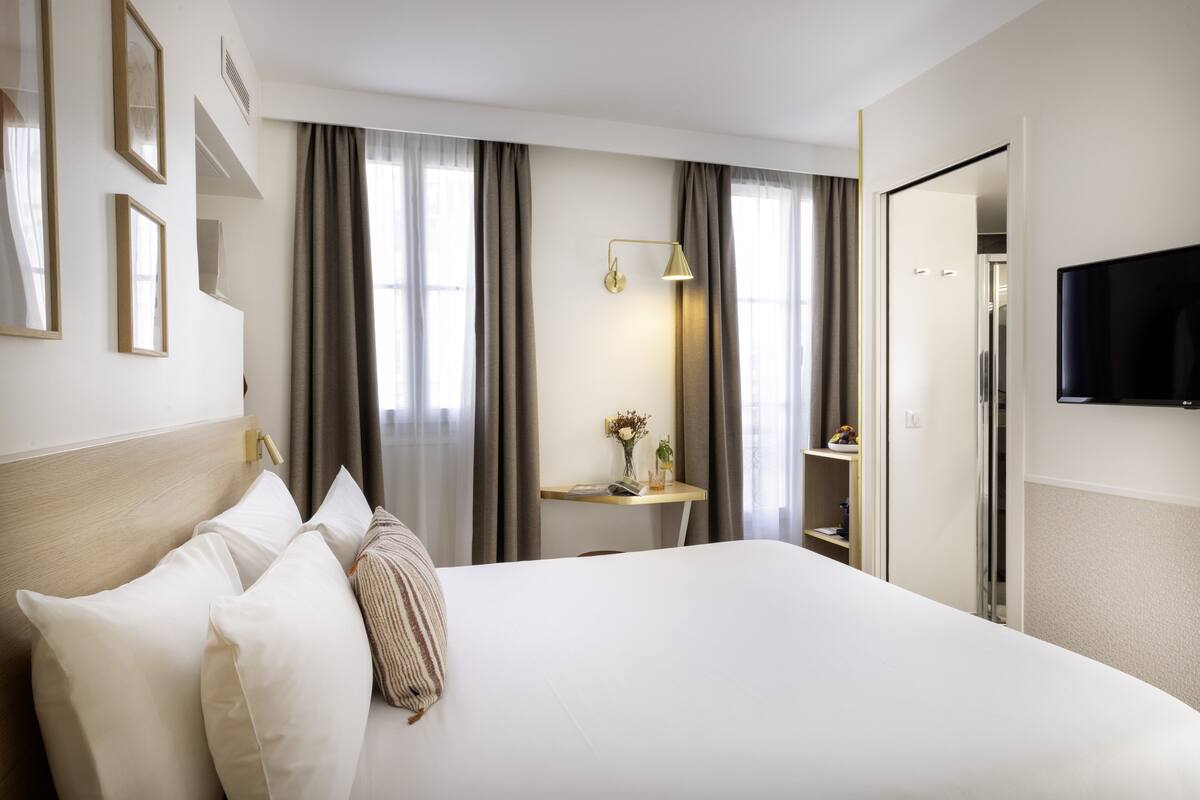 Een hotelkamer met een groot bed, een nachtkastje met een lamp, een aan de muur bevestigde televisie en een kledingkast.