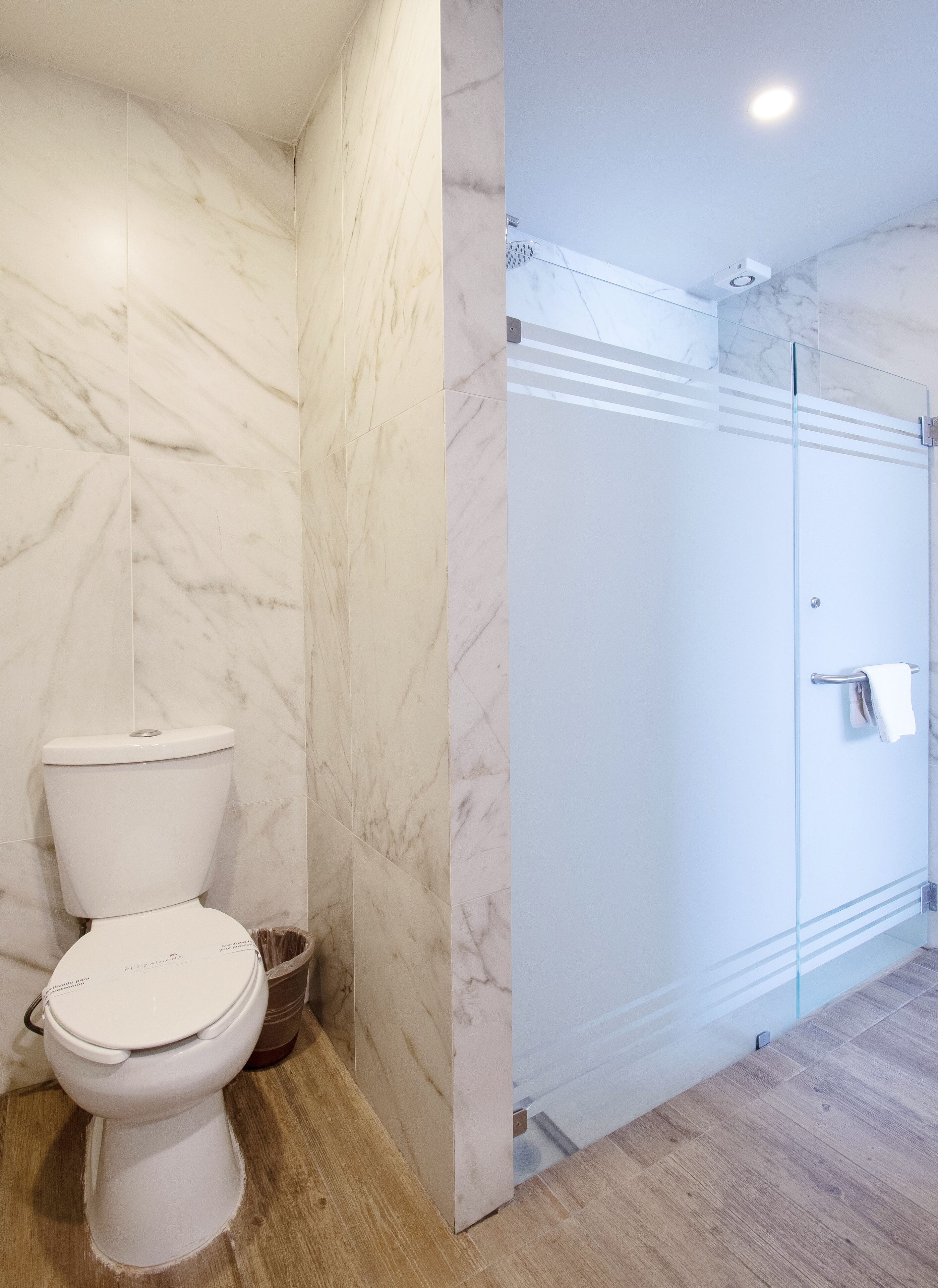 A bathroom with a toilet, a glass shower enclosure, and marble walls.