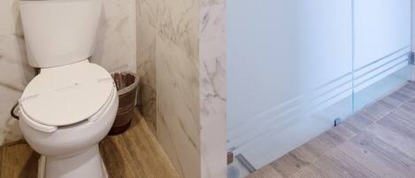 A bathroom with a toilet, a glass shower enclosure, and marble walls.