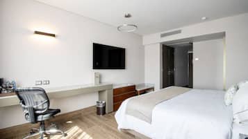 A modern hotel room with a bed, desk, chair, and a TV mounted on the wall.