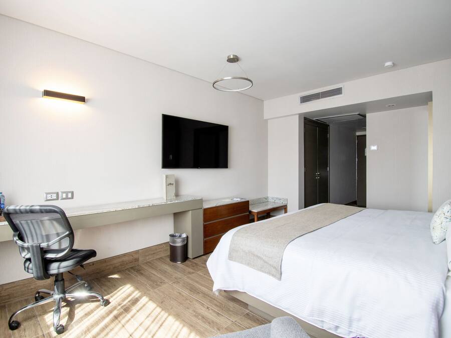 A modern hotel room with a bed, desk, chair, and a TV mounted on the wall.