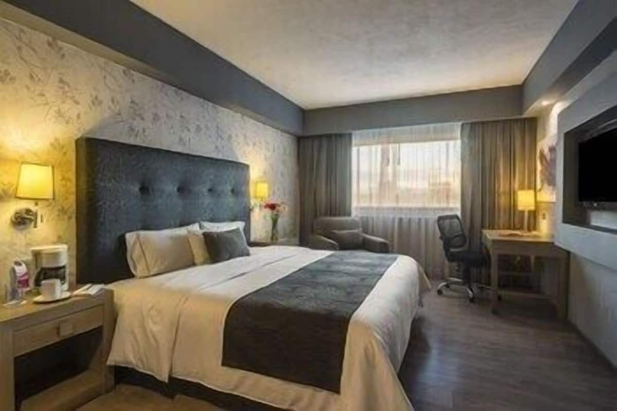 Une chambre d’hôtel avec un grand lit, un bureau, une chaise, une télévision et une fenêtre avec des rideaux.