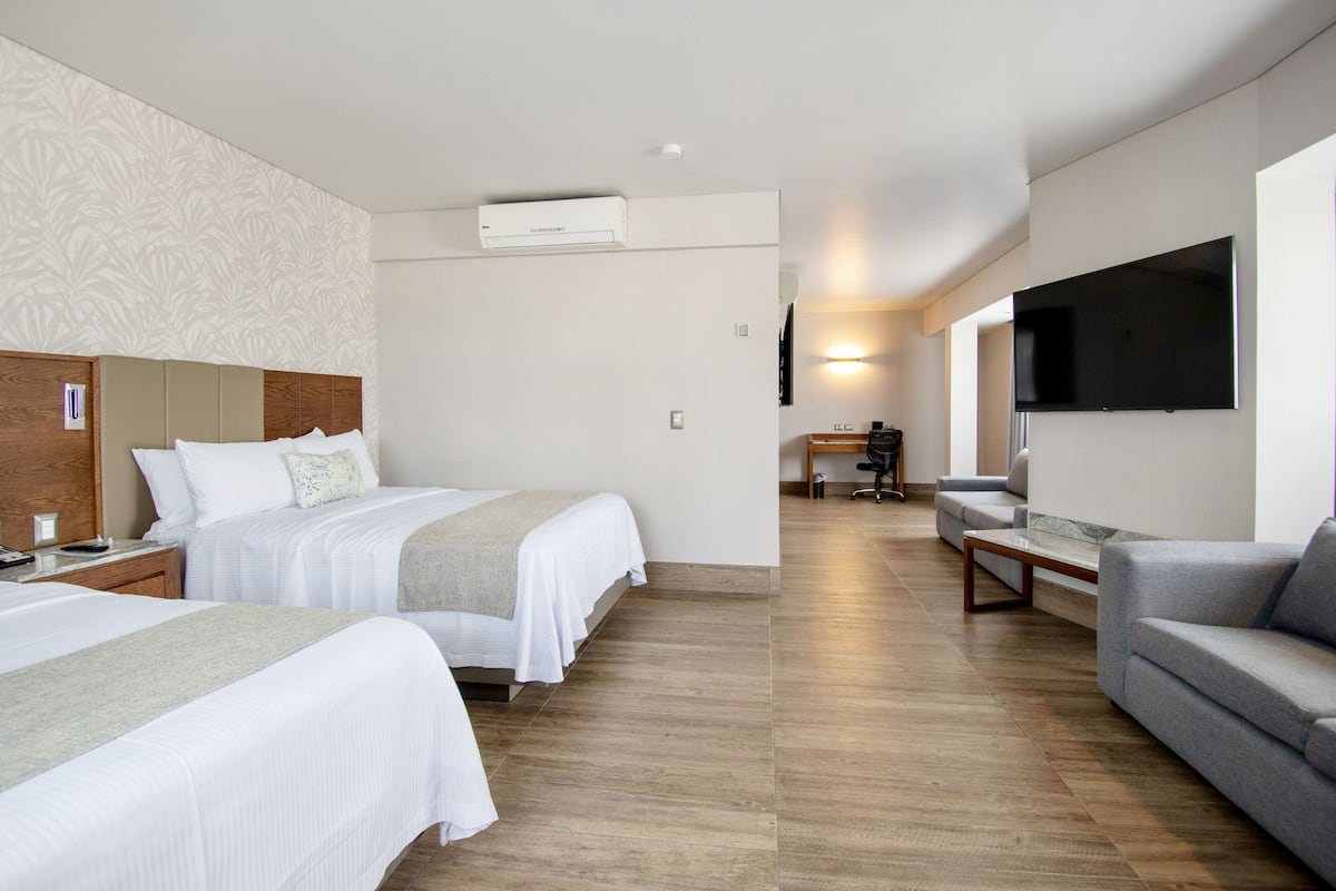 Une chambre d’hôtel avec deux lits, un canapé, une télévision et un appareil de climatisation.