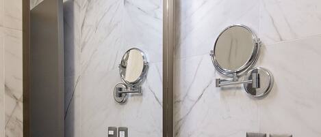 A bathroom with a large mirror, a round mirror, a white sink, and marble walls.