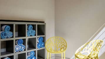 A room with a wooden floor, a built-in shelf with rolled towels, and two yellow chairs.