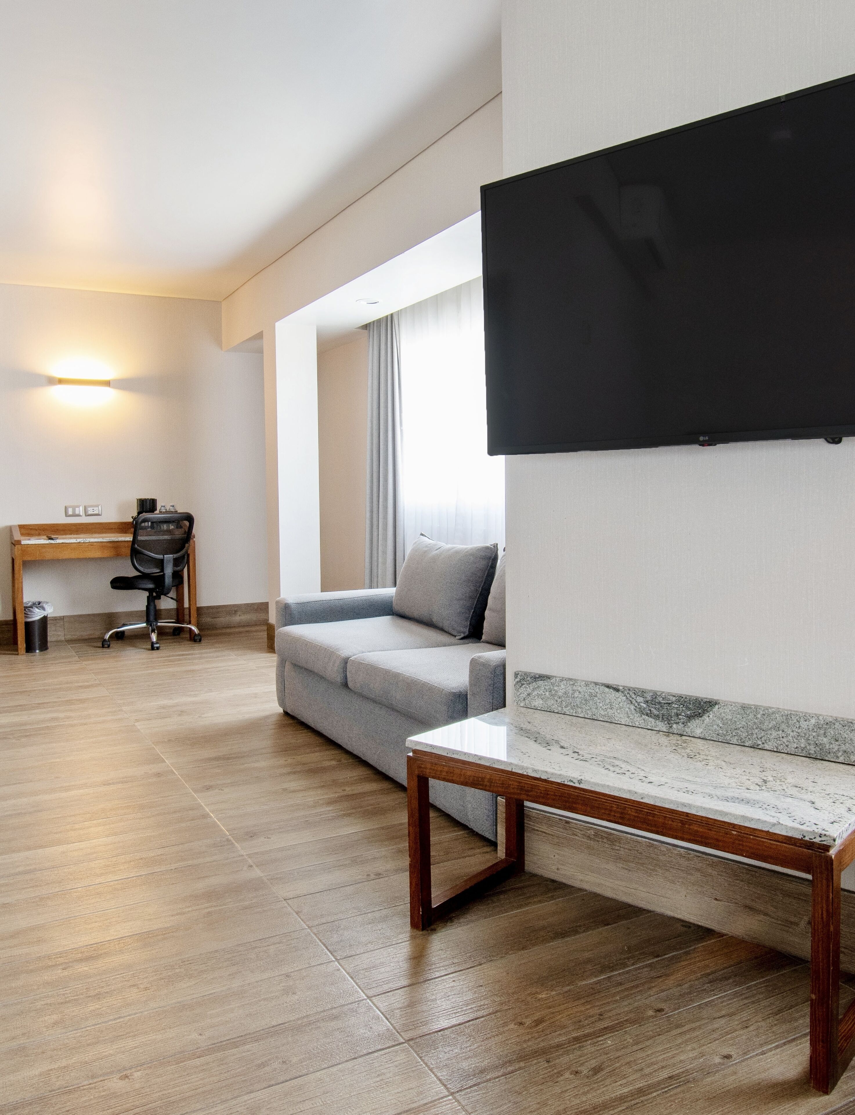 A modern living room with a grey sofa, a wooden coffee table, and a flat-screen TV mounted on the wall.