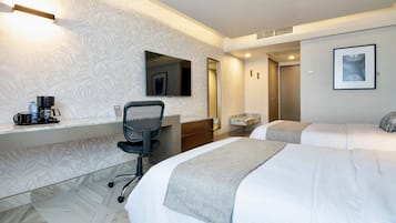 A hotel room with two beds, a desk with a chair, a coffee maker, and a framed picture on the wall.