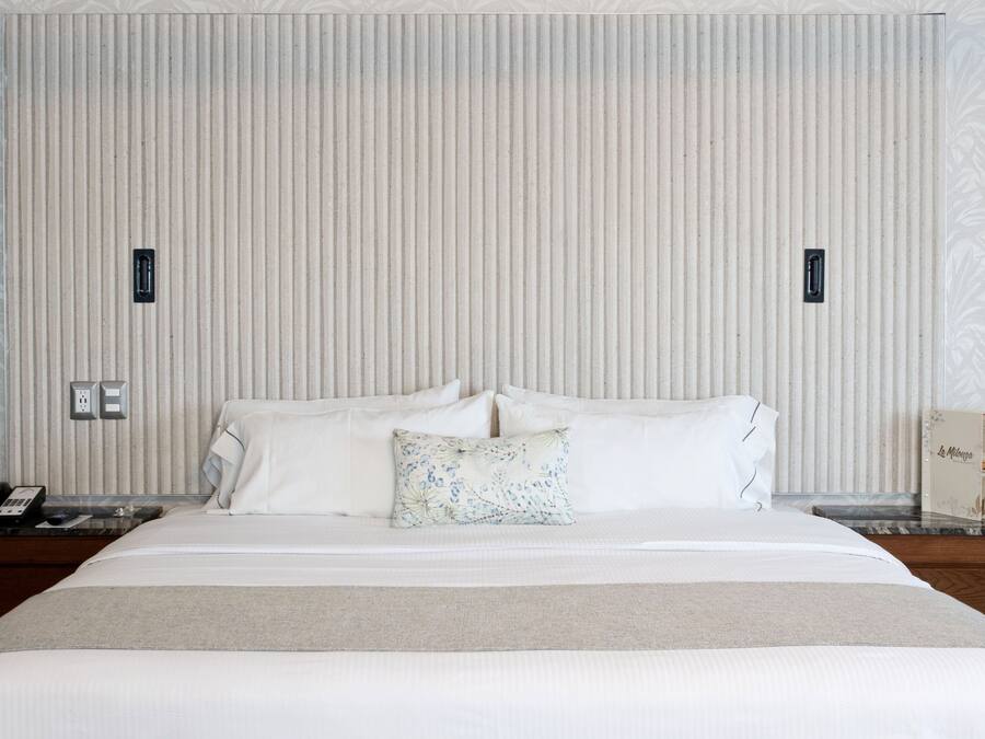 Habitación de hotel con una cama grande, dos mesitas de noche, un teléfono y un objeto decorativo sobre la mesita.