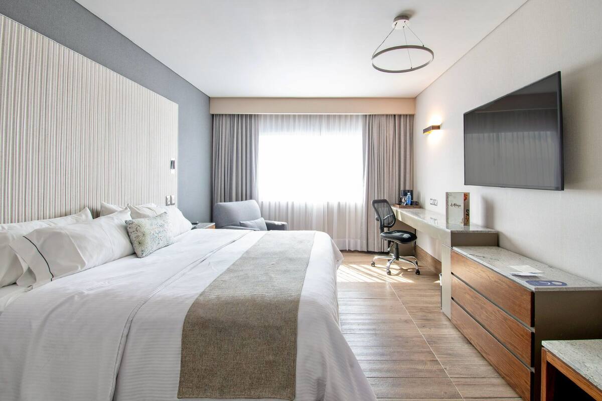 Une chambre d’hôtel moderne, dotée d’un grand lit, d’un bureau, d’une chaise et d’un téléviseur fixé au mur.