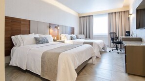 A hotel room with two beds, a desk, a chair, and a large window with curtains.